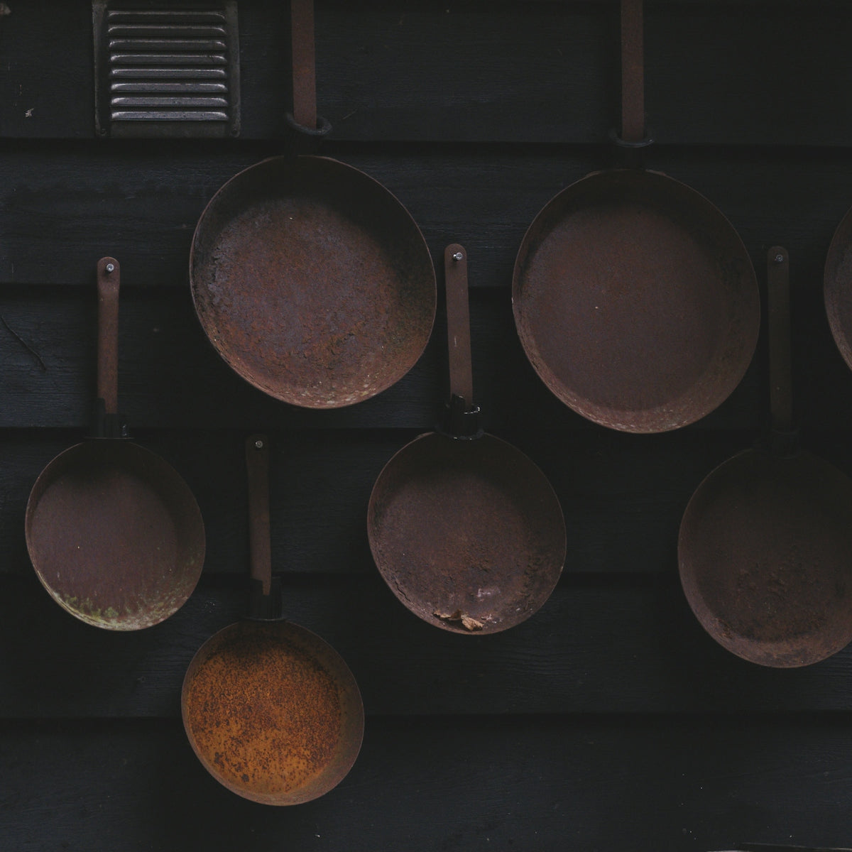Several old copper pots hanging on a dark wall